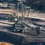 Large bucket wheel excavator operating in an open-pit mine with layered soil and coal.